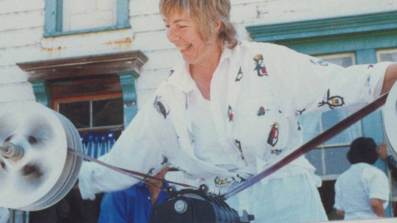 A woman in short blonde hair and a white top spools 35mm film through an editing machine.
