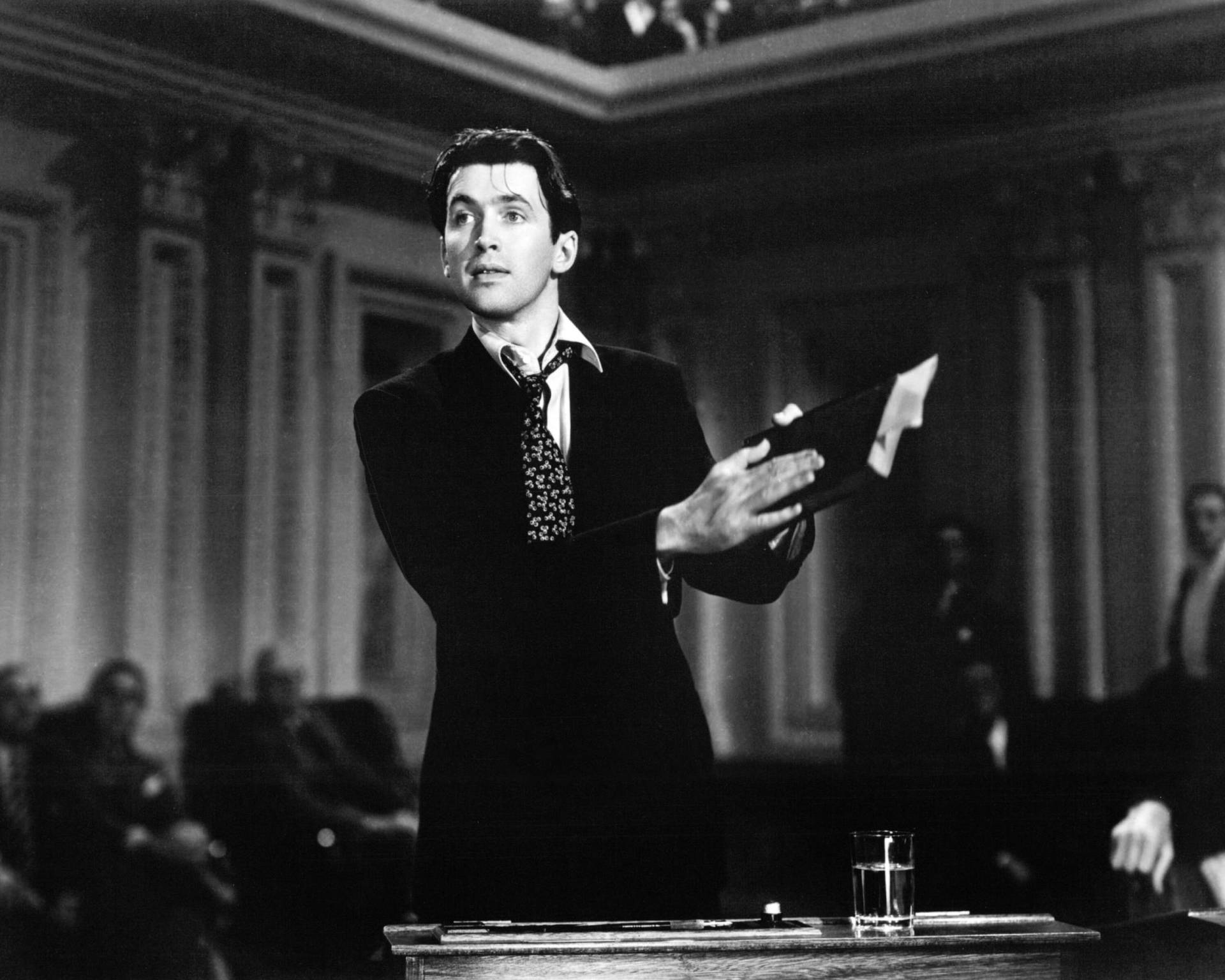 Black and white image of Jimmy Stewart speaking passionately and looking disheveled in a movie scene.