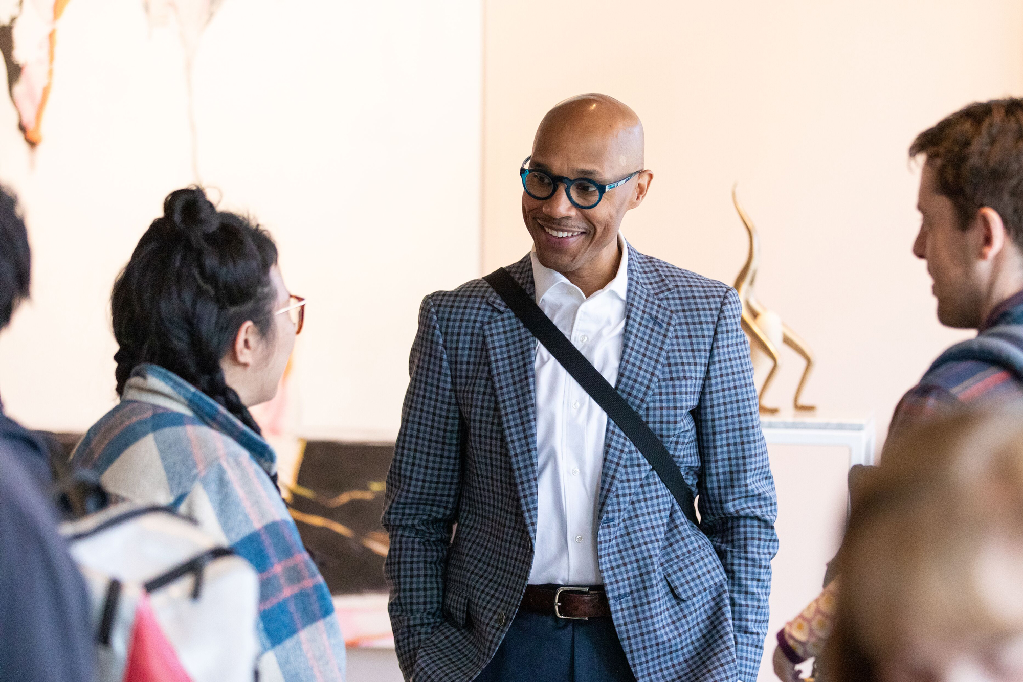 smiling Black man in suit and glasses talks to people at an event