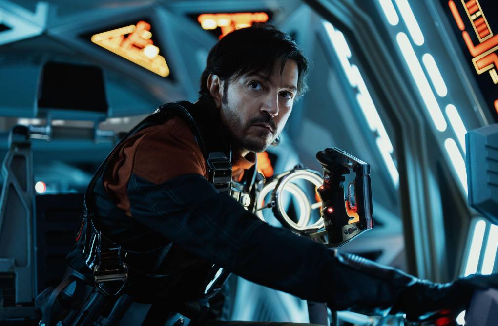 A man in a flight suit glances up nervously. He is in a futuristic looking space ship.