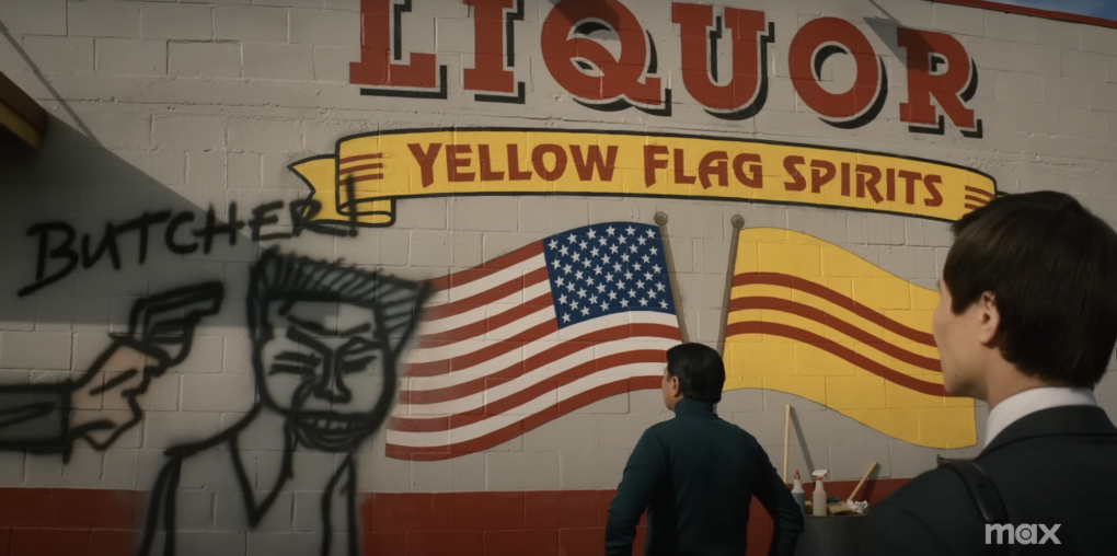 Two men stand staring at a wall featuring the word LIQUOR, plus American and South Vietnamese flags. There is graffiti on the wall depicting the shooting of Nguyen Van Lem.