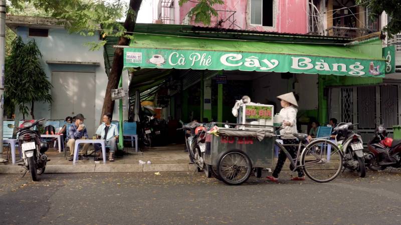 A wide shot of two men sitting at a cafe in Vietnam. 