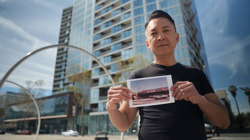 Portrait of Asian man holding an old photograph in front of a sleek apartment building.