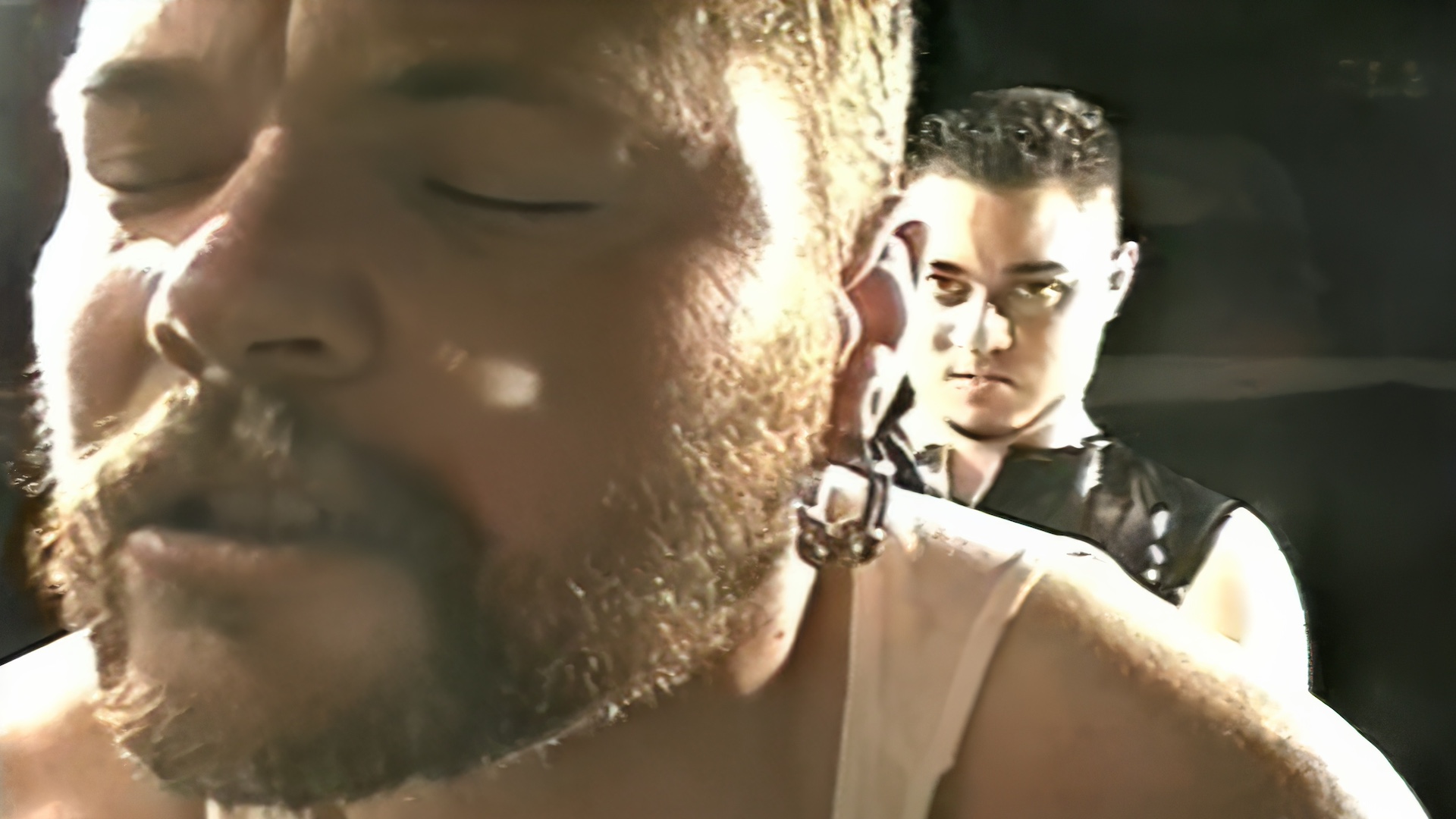 extreme close-up of bearded person's face, eyes closed, with another person behind