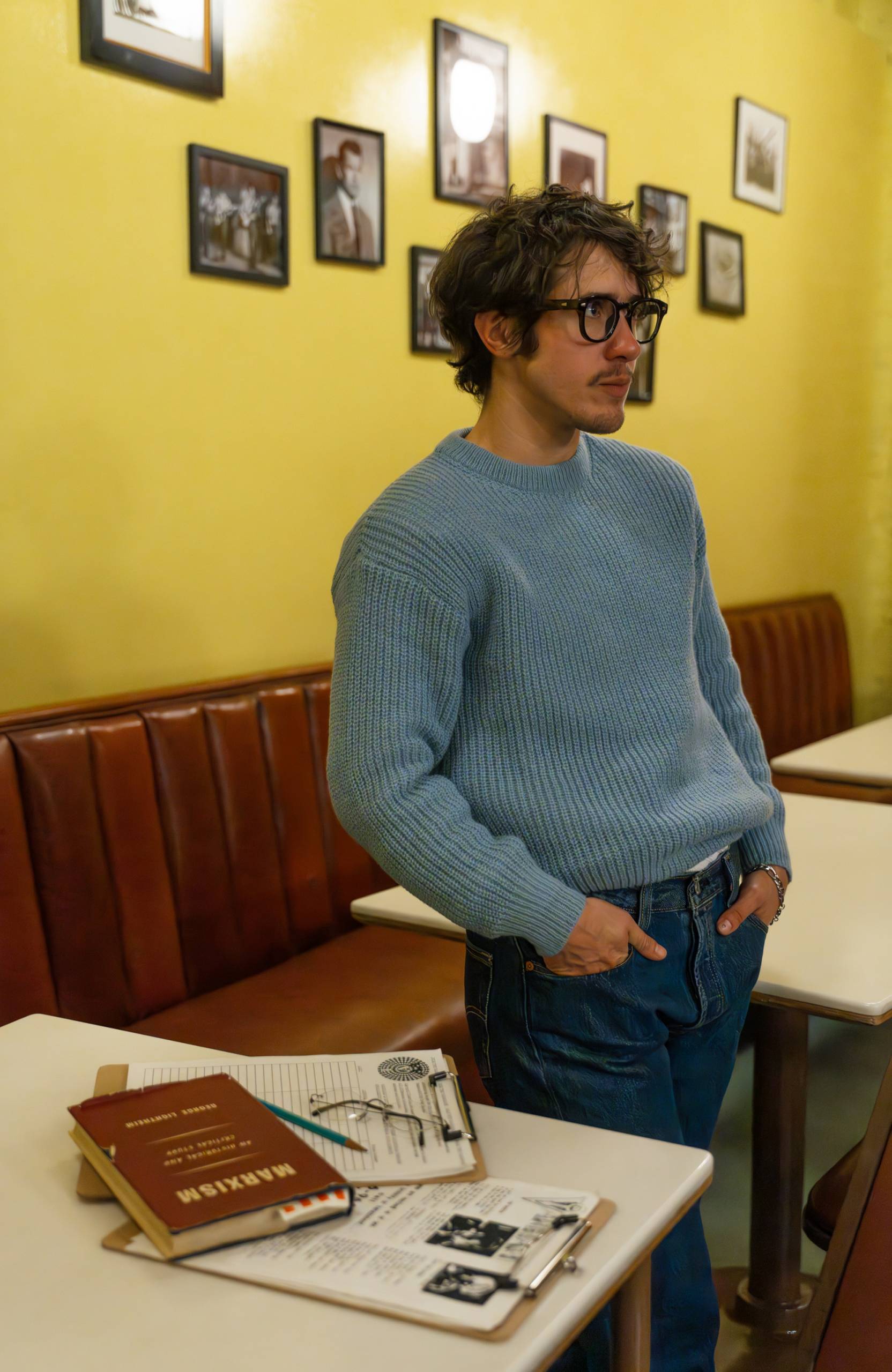 A young man in glasses and a sweater stands next to his copy of 'Marxism.'