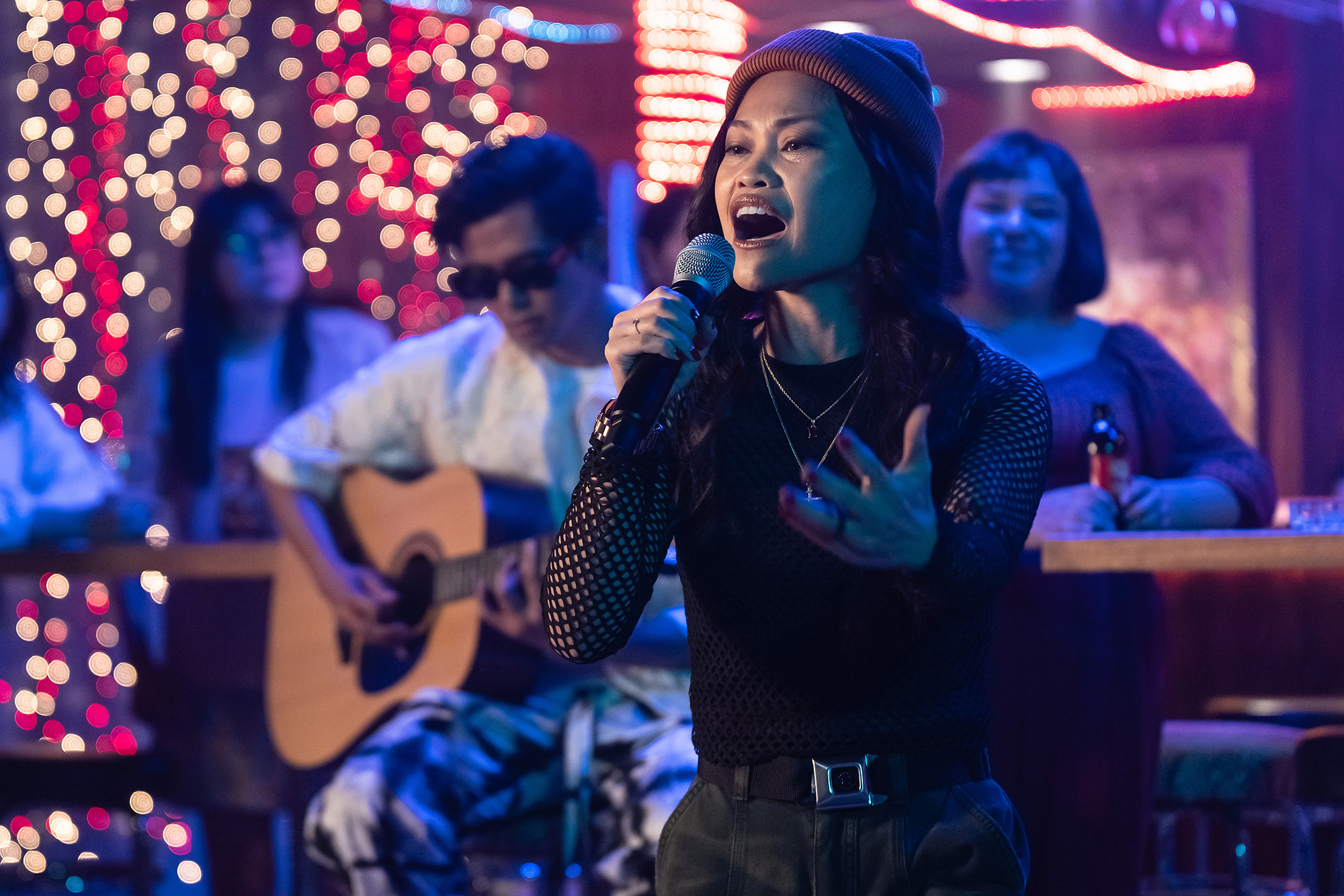 A young FIlipina woman in a beanie and mesh top holds a microphone at a custom-lit party