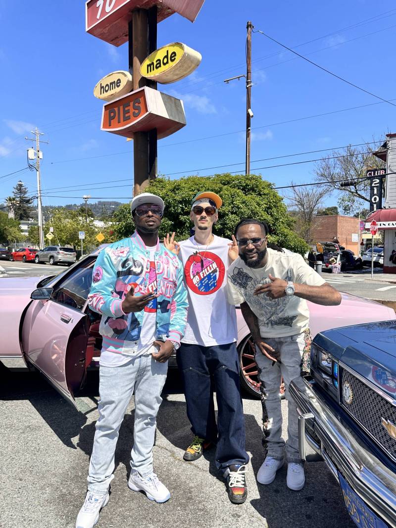 Three people pose for a photo in a parking lot