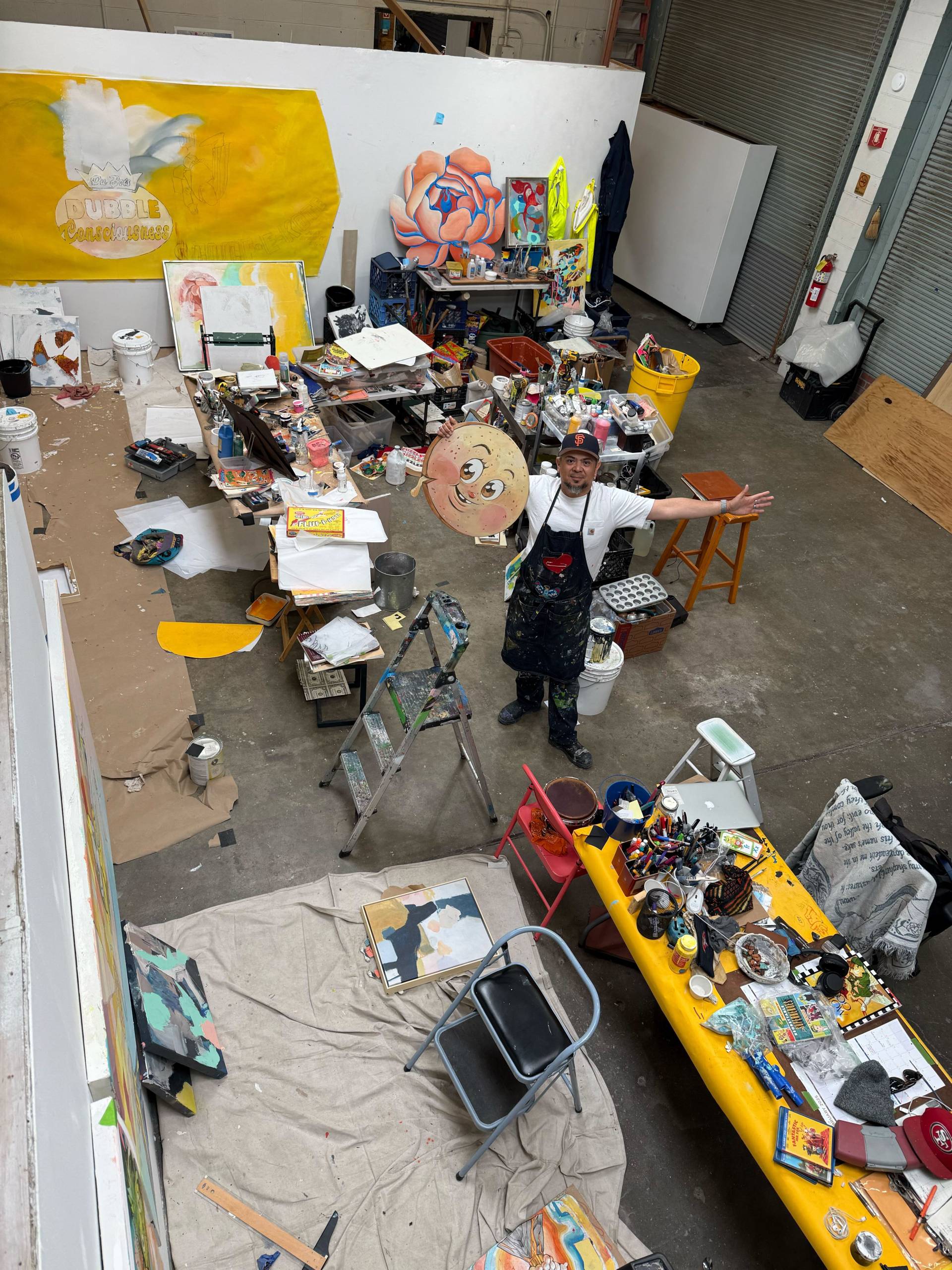 An overhead view of a man standing in a studio populated by arts supplies.