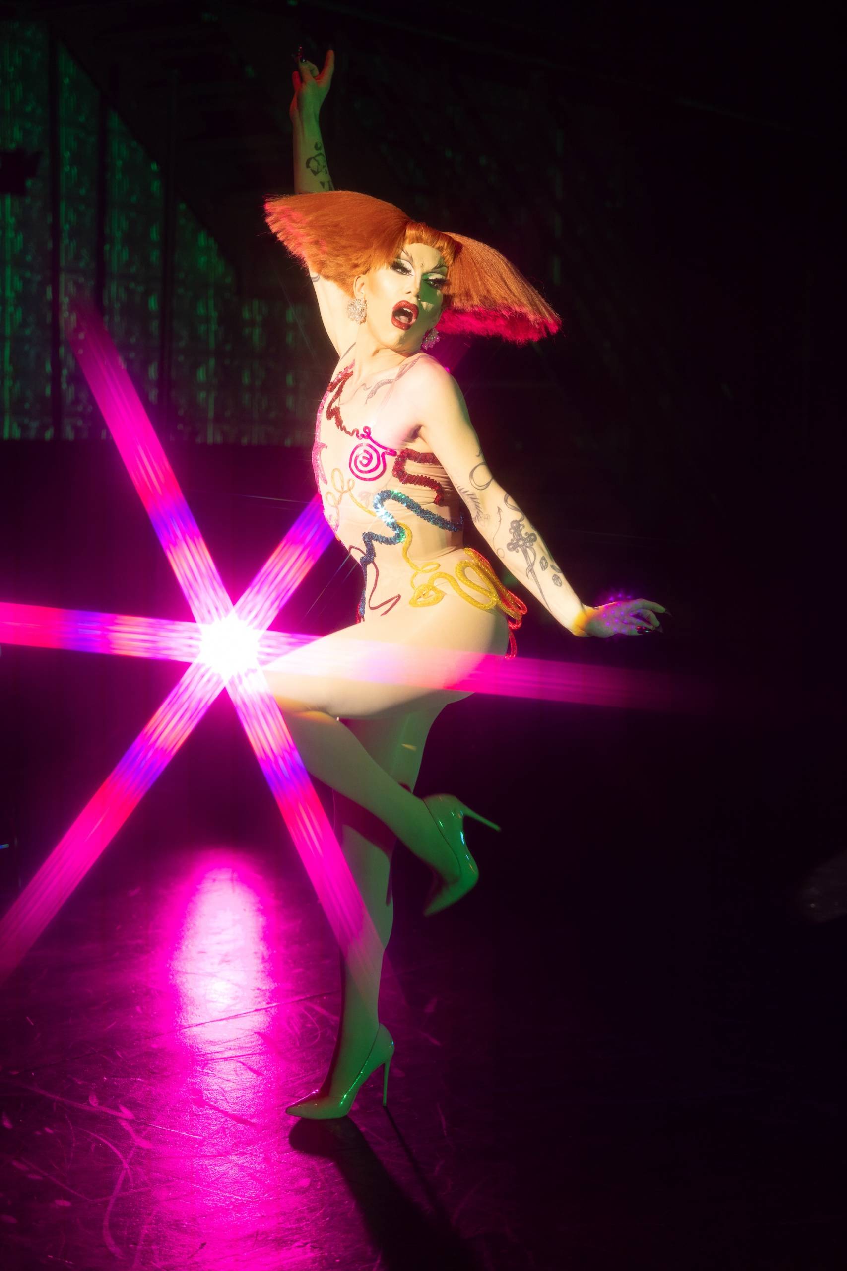 A drag performer with a sharp, exaggerated bob and pop art-style bodysuit.
