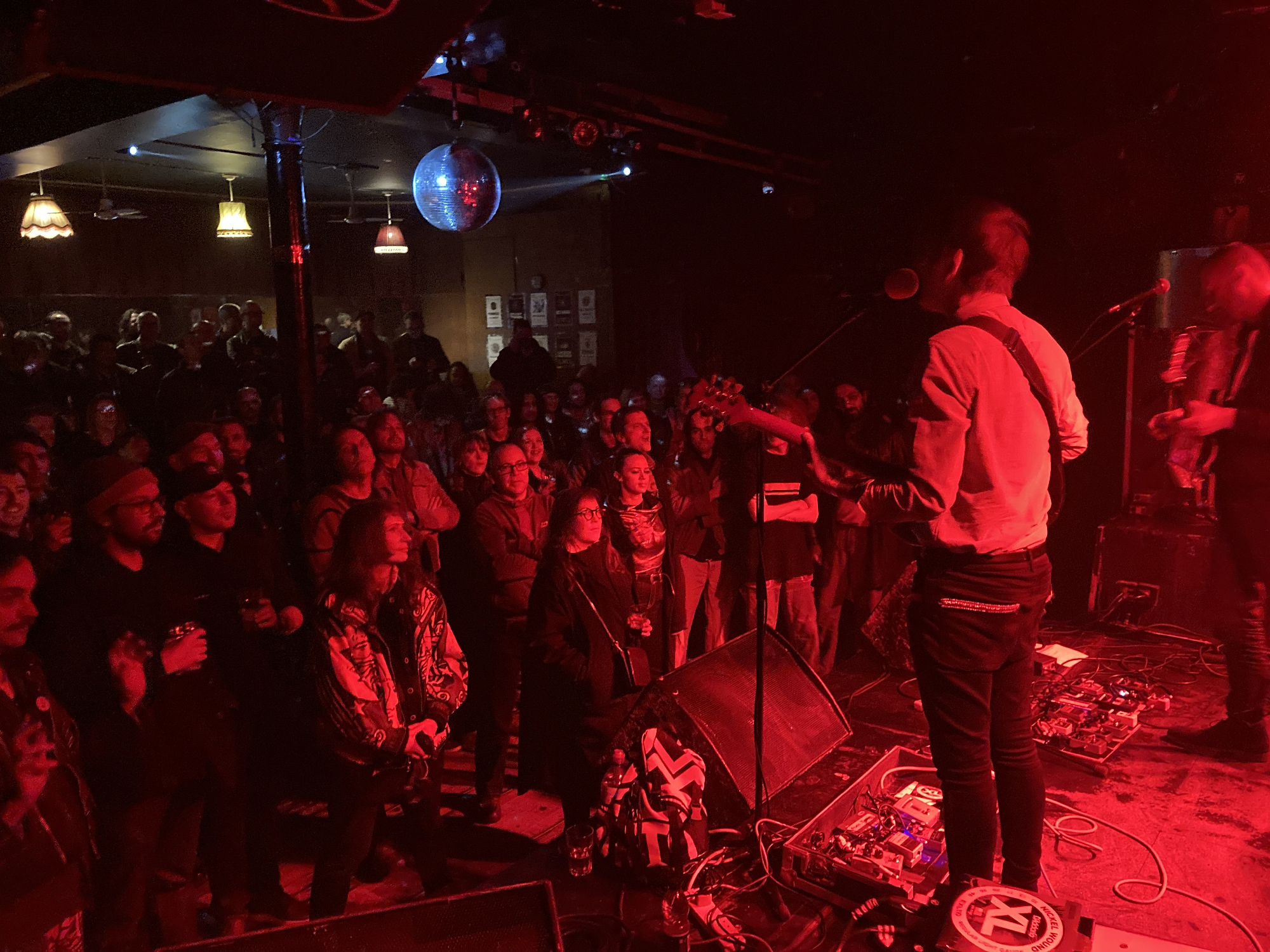 person on stage with guitar in front of red-lit small crowd