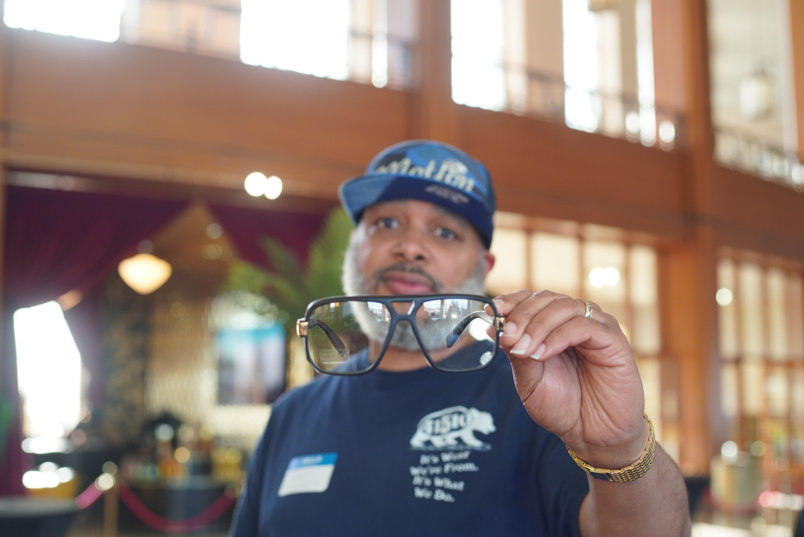 A man poses for a photo while holding a pair of glasses toward the camera.