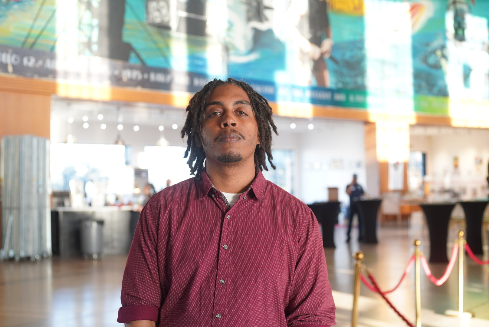 A man in a red dress shirt stands and poses for a photo.