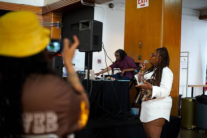 A woman in all white holds a microphone as she rocks a crowd.