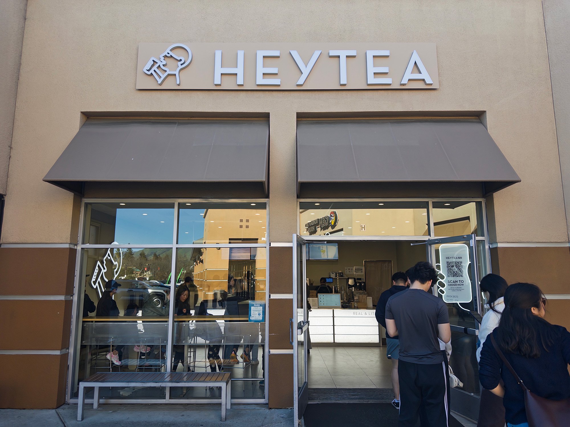Facade of a busy boba shop, with a line of people waiting outside the entrance. The sign above reads, "HEYTEA."