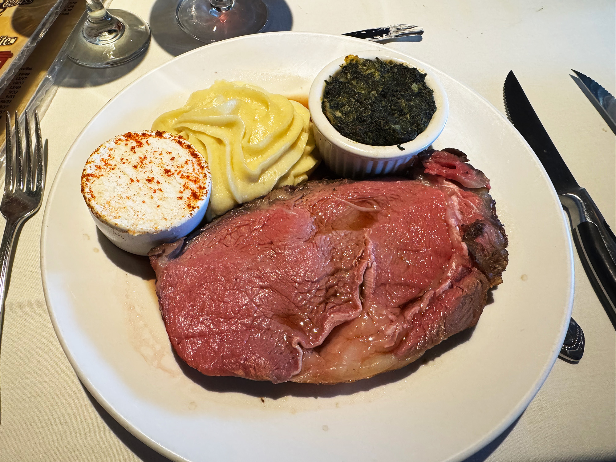 Prime rib cooked quite pink and rare on a white place with mashed potatoes and creamed spinach.