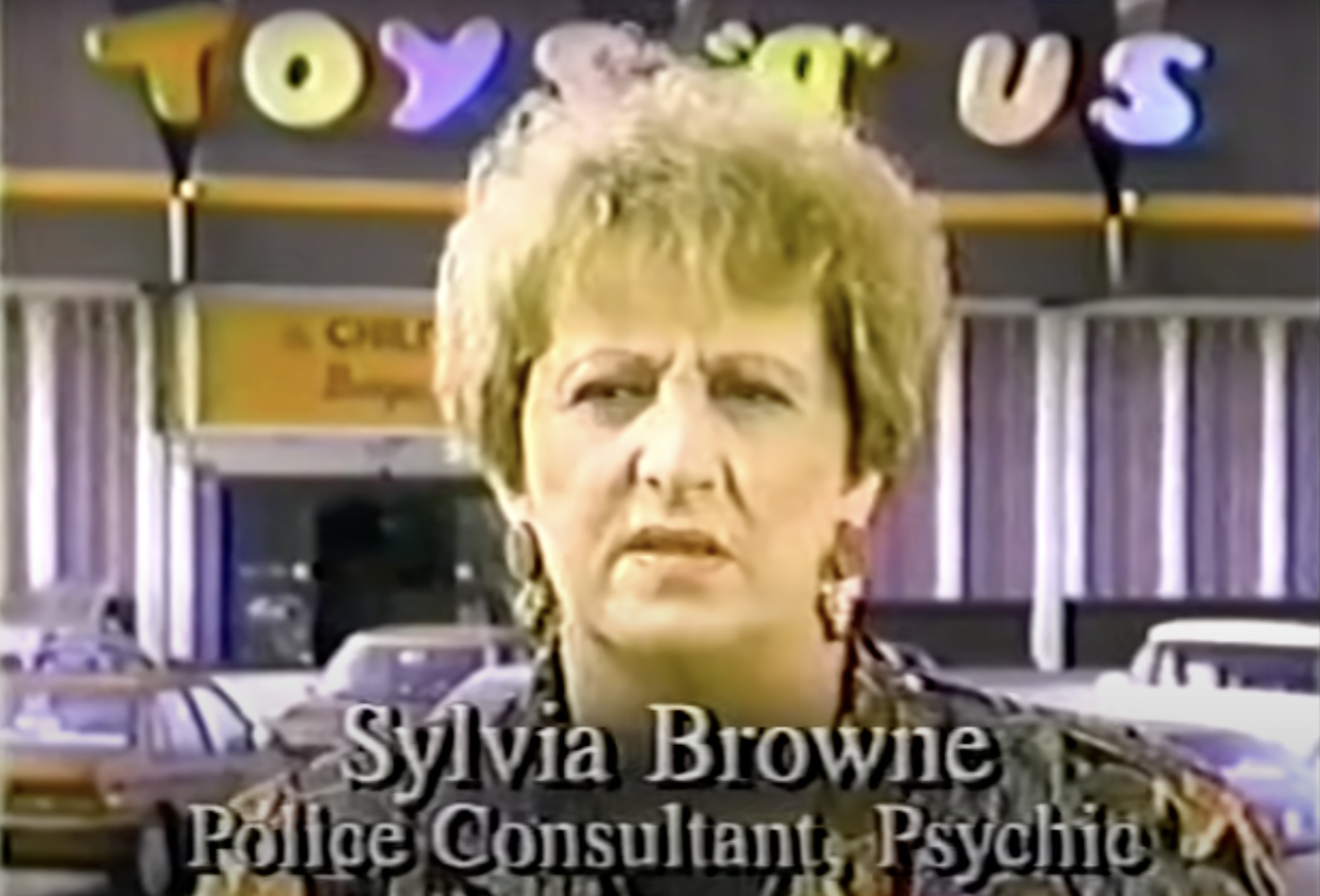 A white senior woman with short brown hair stands in front of a Toys ‘R’ Us store.