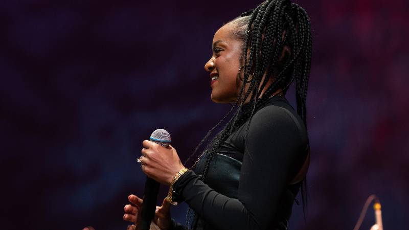 A Black woman in braids and a black top holds a microphone, in profile