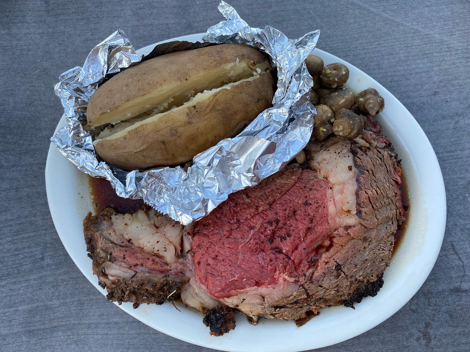 Overhead view of a bloody-centered slab of prime rib and a foil-wrapped baked potato.