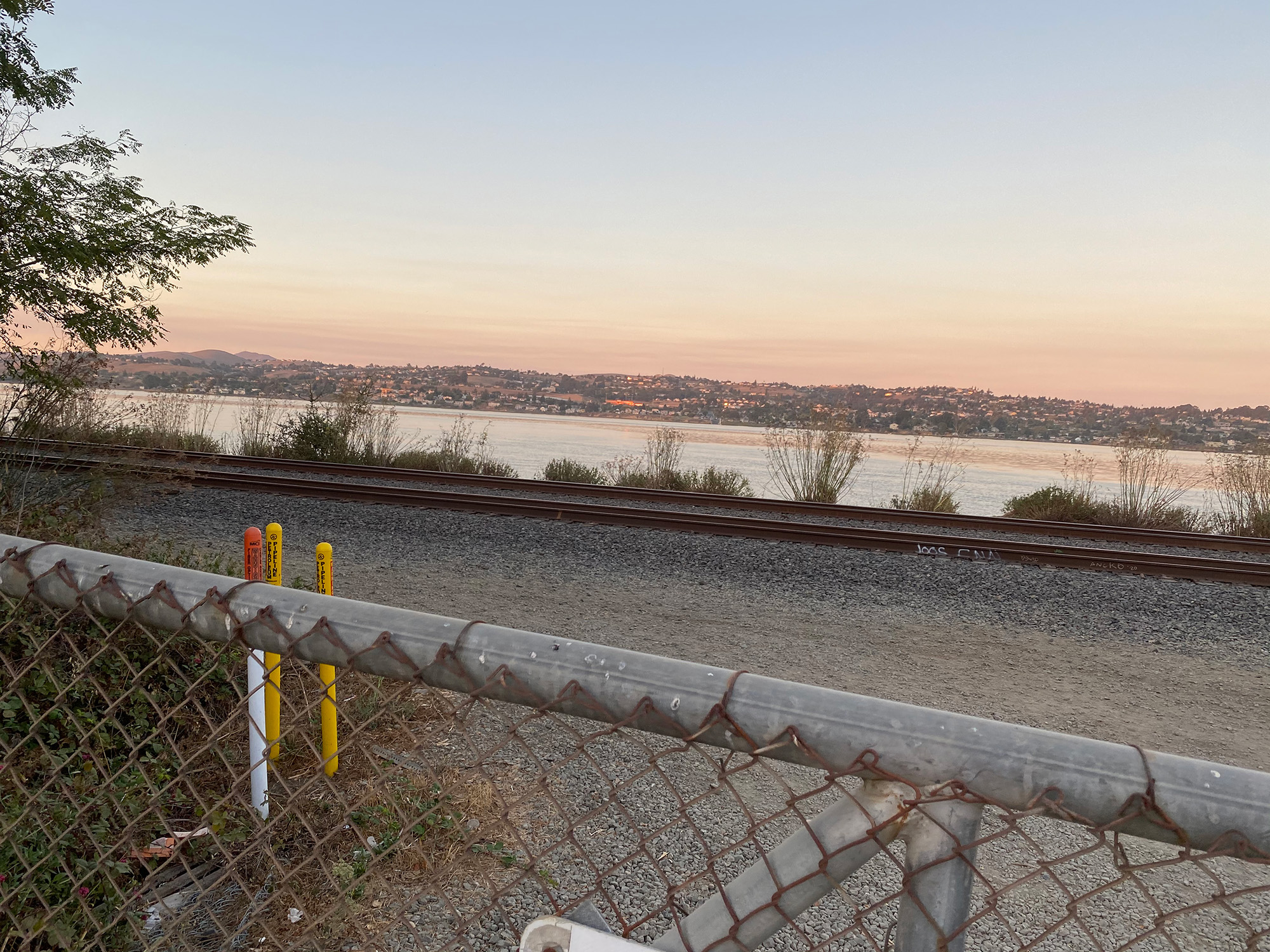 View of a sunset over the waterfront, from the other side of a chain link fence.