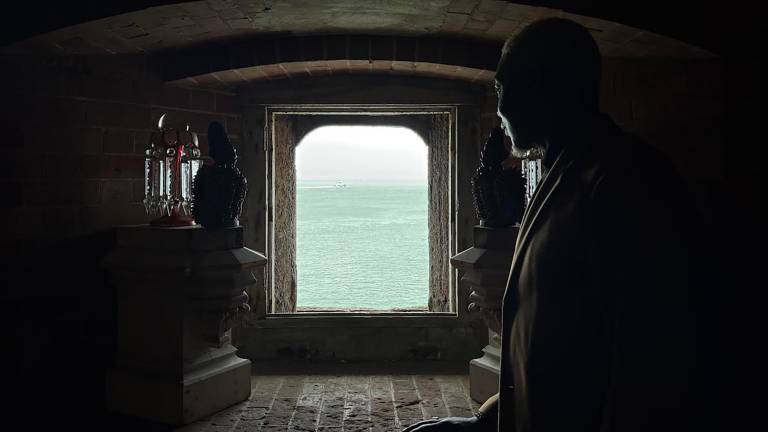 An open window looks out into the San Francisco Bay waters as the backlit silhouette of a man looks outward.