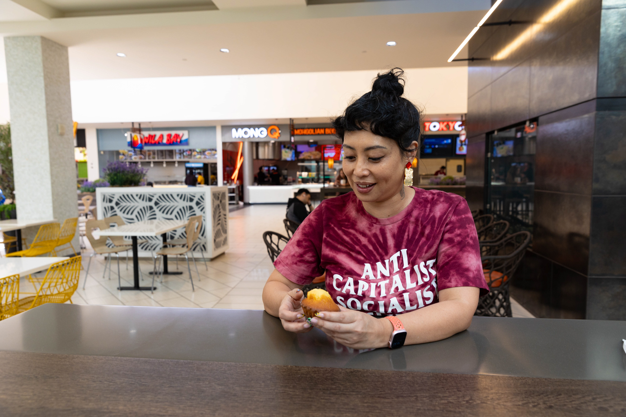 A woman sits in a mall foot court holding a madeleine cake.
