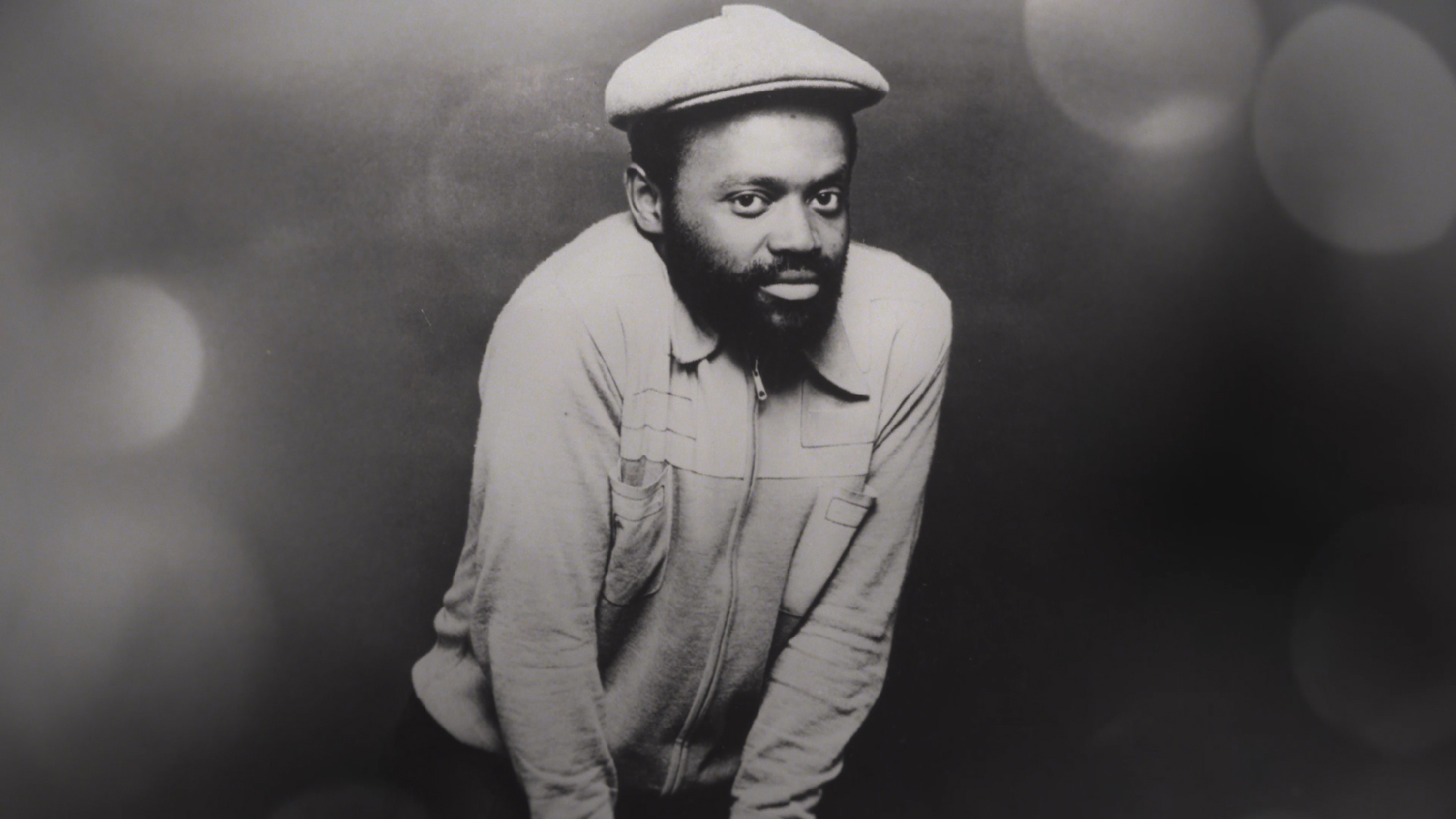 black-and-white photo of young Black man with beard in crouch pose