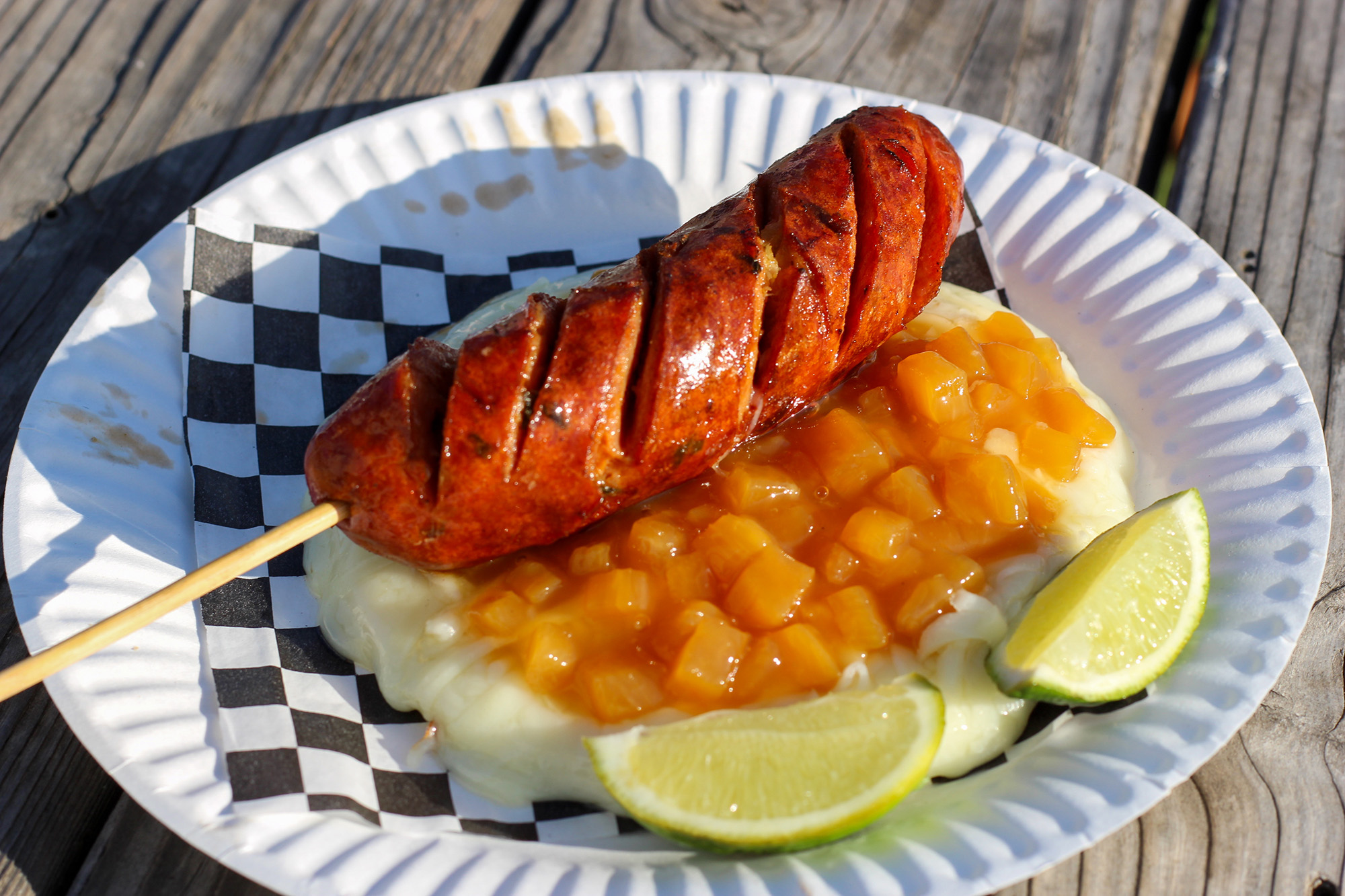Arepa topped with chopped pineapple and a sausage link.