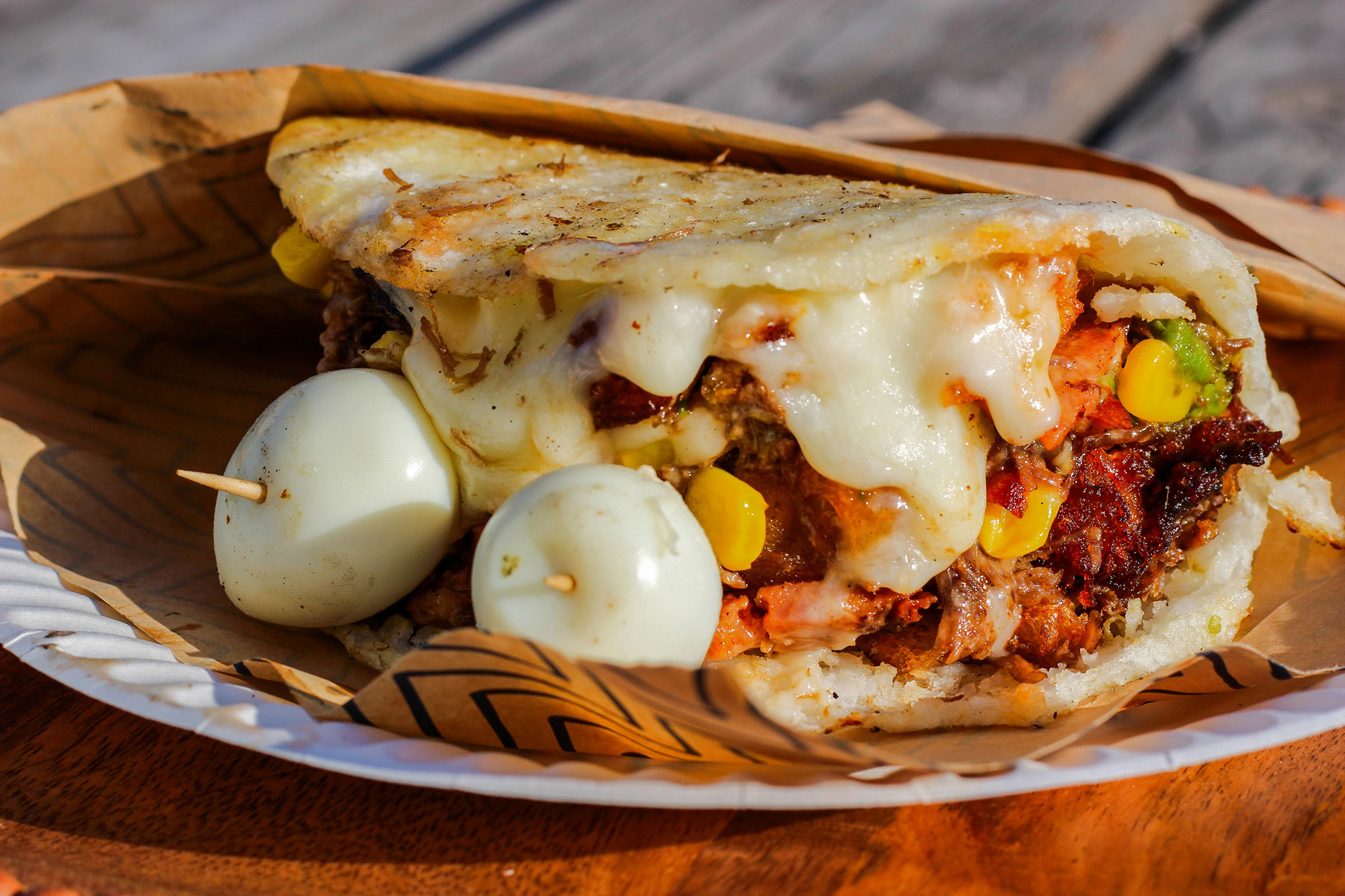 A cheesy, overstuffed arepa on a paper plate.