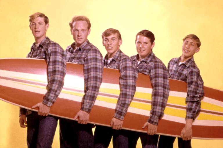 five young men in plaid shirts hold a long surfboard