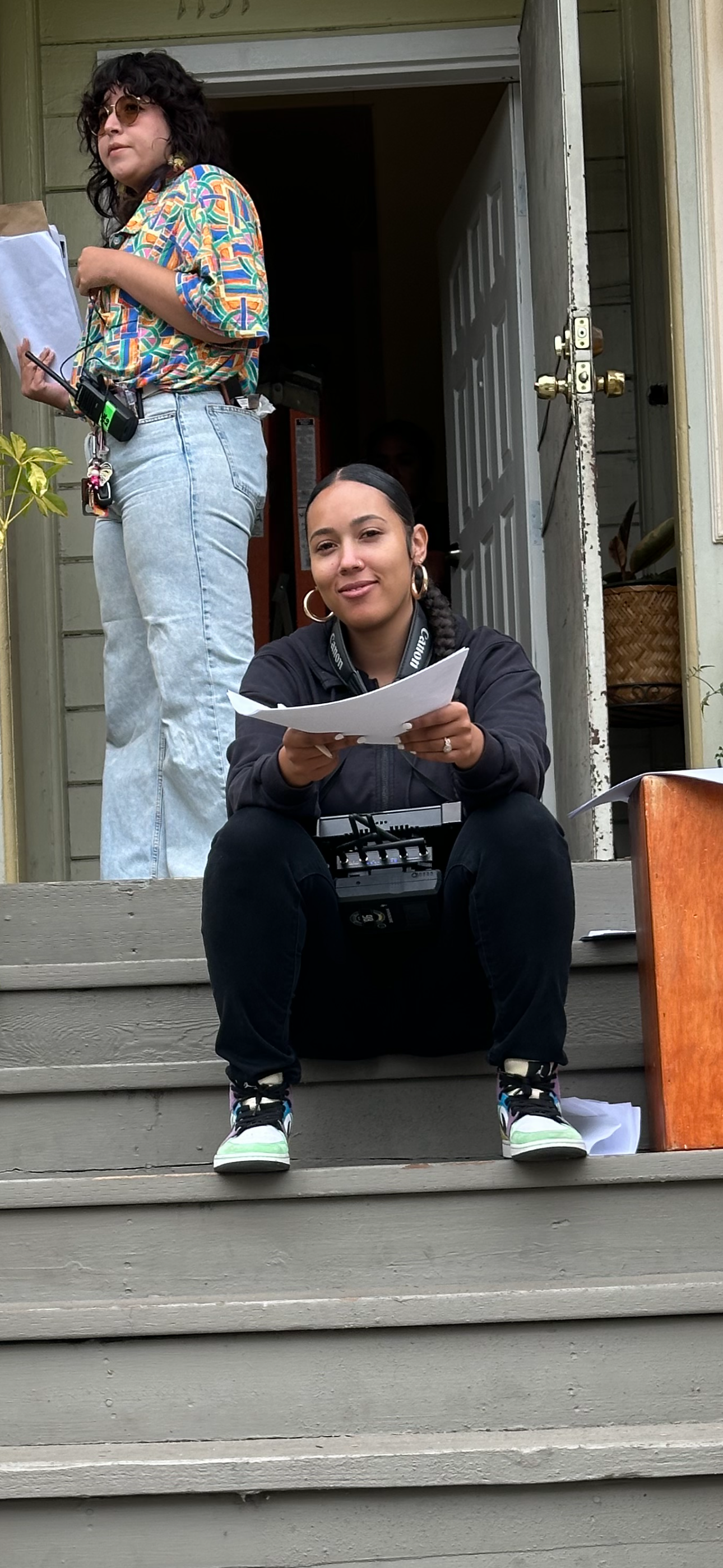 A woman in all back clothing, sitting on a set of stairs while holding a printed script for a film.
