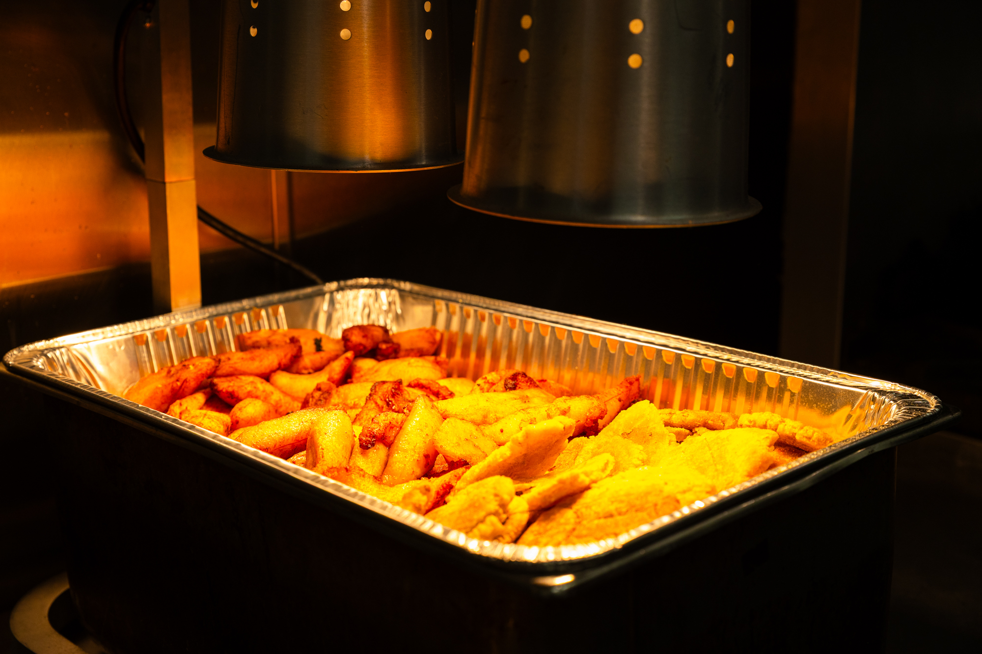 A tray of fried plantains under a heat lamp.