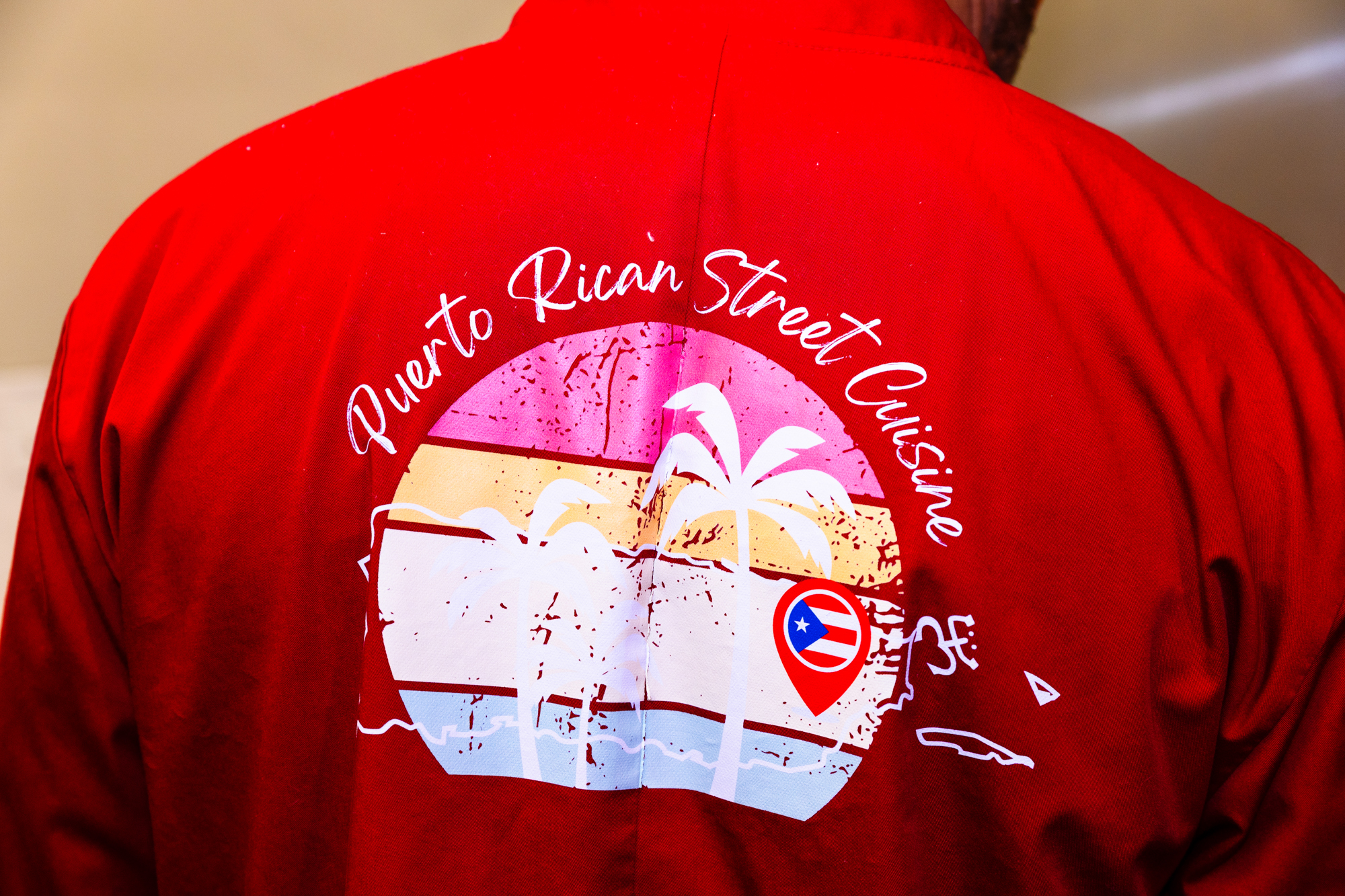 The back of a red chef's jacket. The text above the palm tree logo reads, "Puerto Rican Street Cuisine."