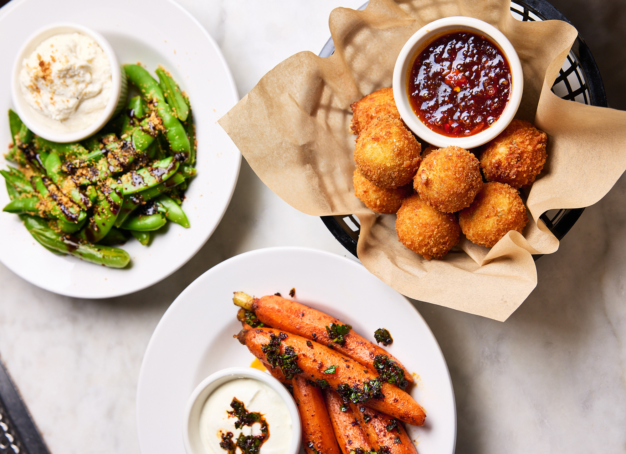 Overhead view of three appetizers: sugar snap peas, carrots, and croquettes.