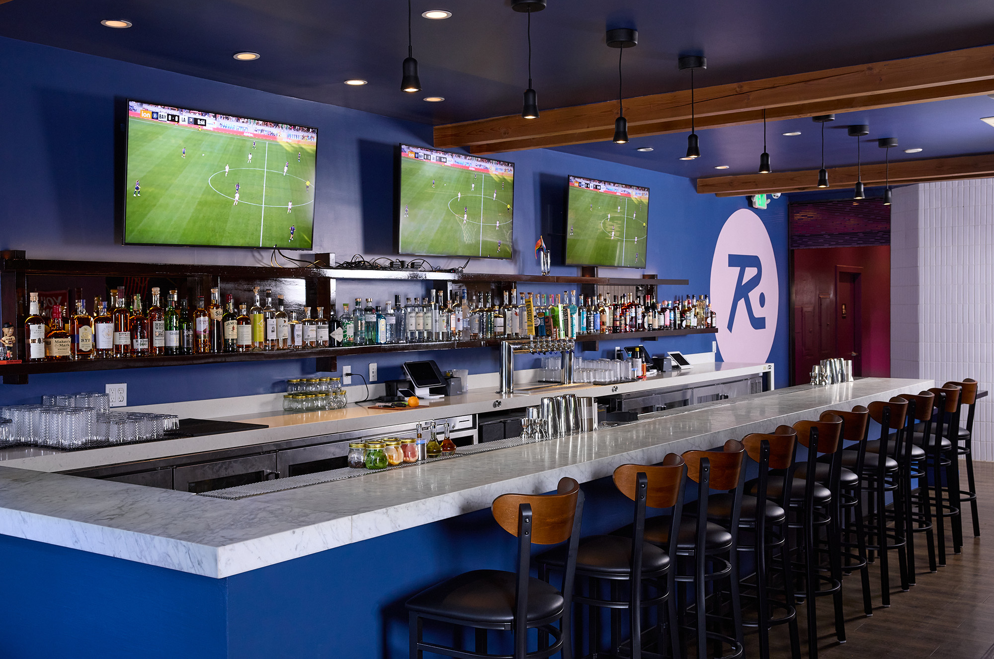 Bar counter with TV screens behind it showing a soccer game.