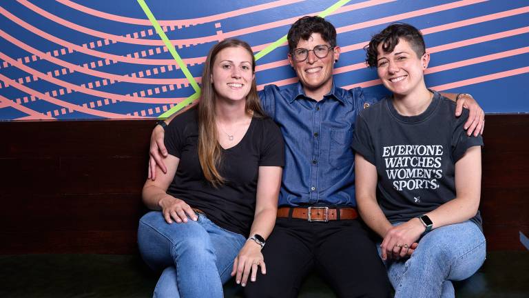 Three women pose for a portrait while sitting on a sofa.