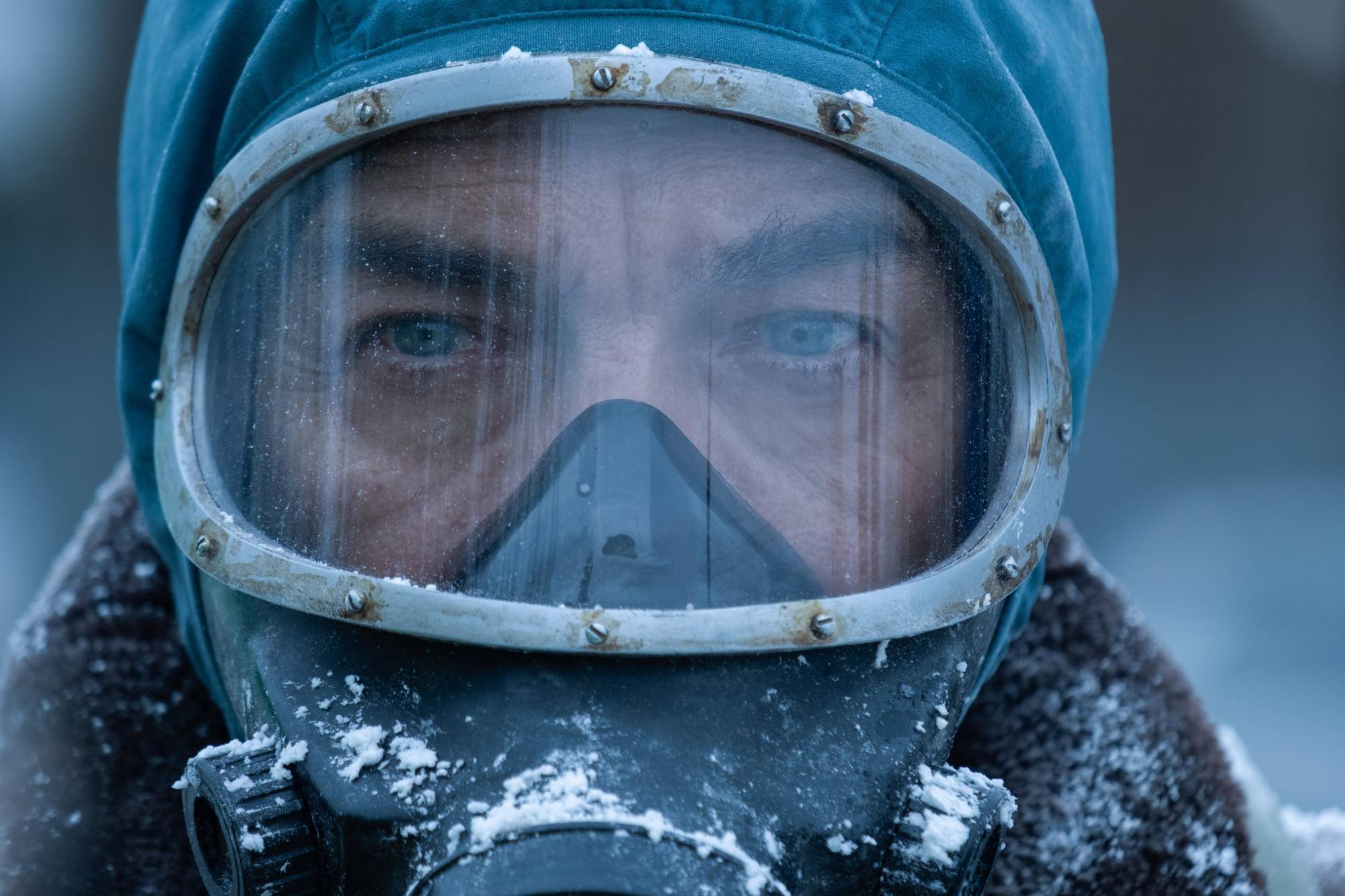 A close up on a man's eyes, his face hidden beneath a hooded gas mask of some kind.