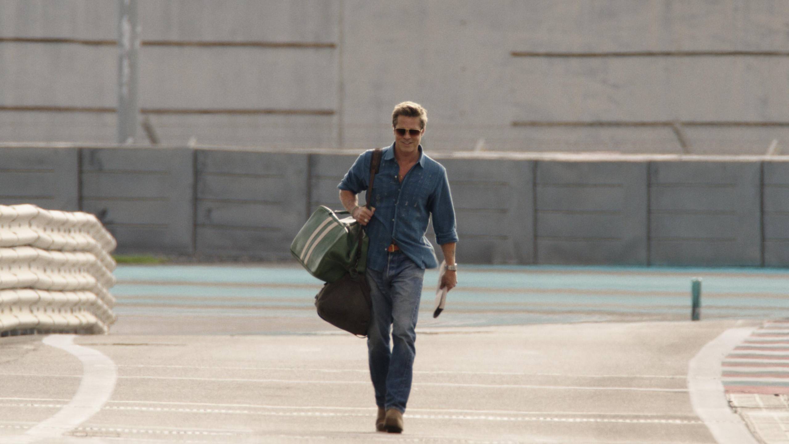 white man carries bags, looks cool, on racetrack