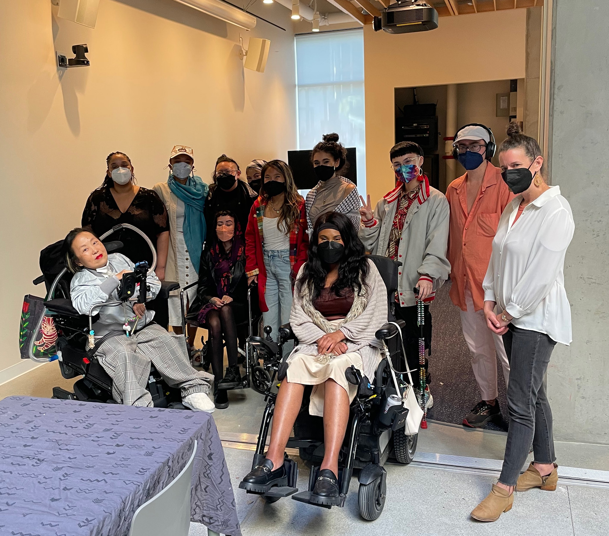 A large group of nearly a dozen people, all wearing masks and some using wheelchairs, stand in a hallway of a partially finished building