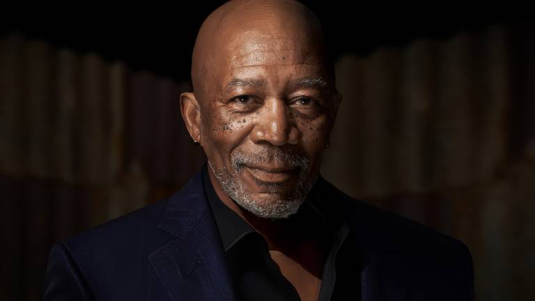 An older Black man in a stylish suit smiles and looks into the camera