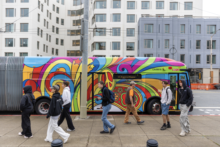 A city street with a San Francisco Muni bus decorated with colorful 1970s psychedelic graphics.