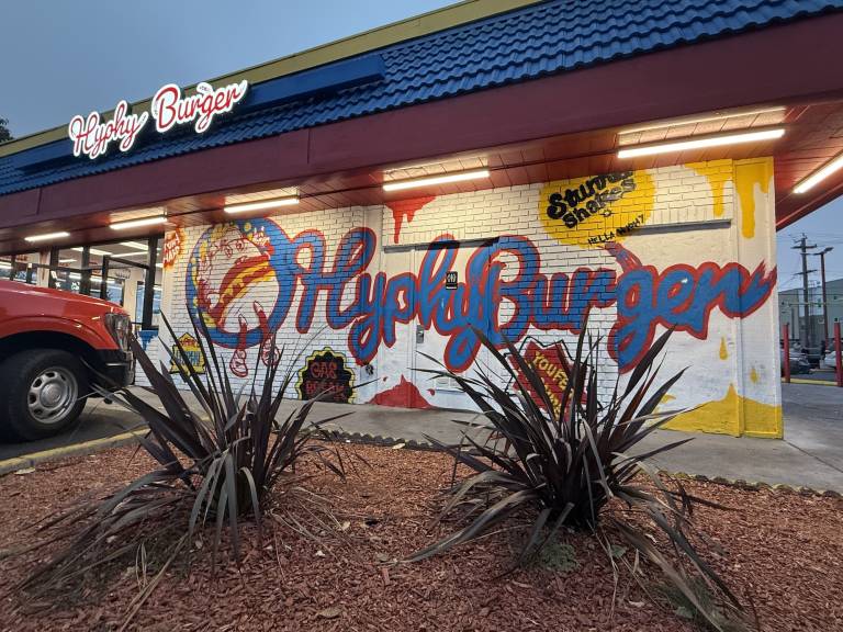 The words "Hyphy Burger" are written in blue lettering on a white background of a restaurant.