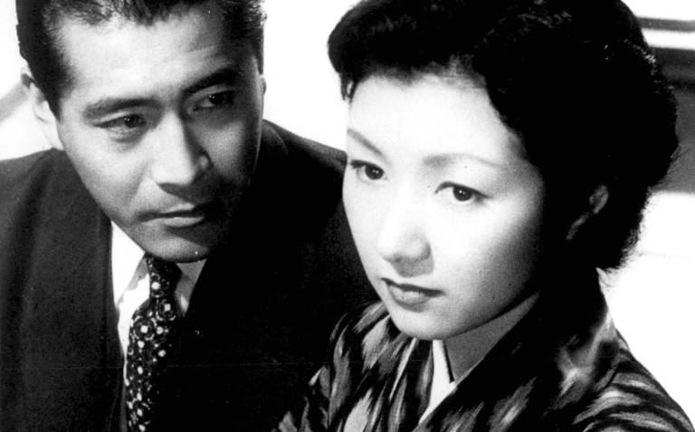 A black-and-white image of a well-groomed Japanese man in a suit and tie gazing upon an attractive young Japanese woman.