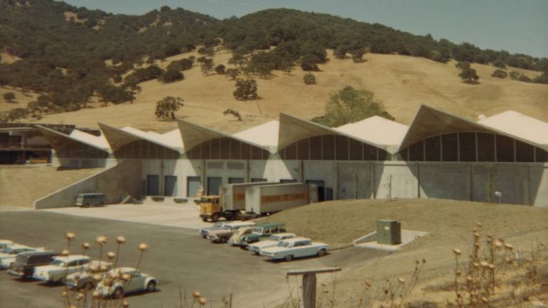older photograph of pointed warehouse roof with 50s and 60s cars parked outside