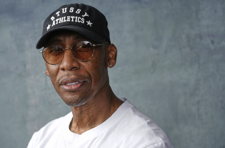 A Black man wearing a baseball cap and white t-shirt in close-up.