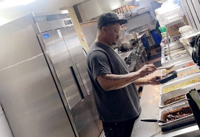 A chef ladling food into a tray inside a restaurant kitchen.