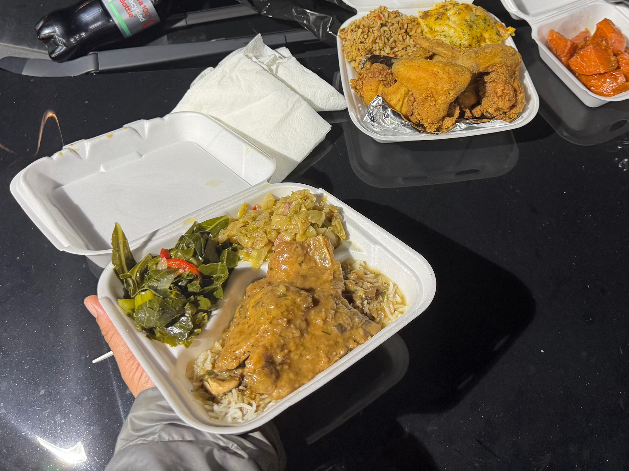 Takeout containers loaded with soul food — smothered pork shops, green beans, fried chicken — on the hood of a car.