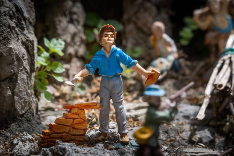 A small figurine faces forward and lays bricks at the center of a diorama.