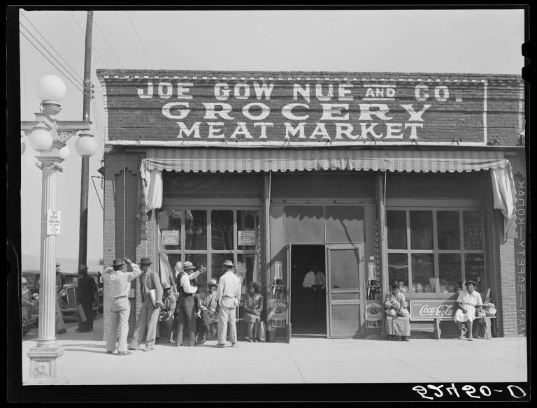 black-and-white image of small crowd on sidewalk outside of building