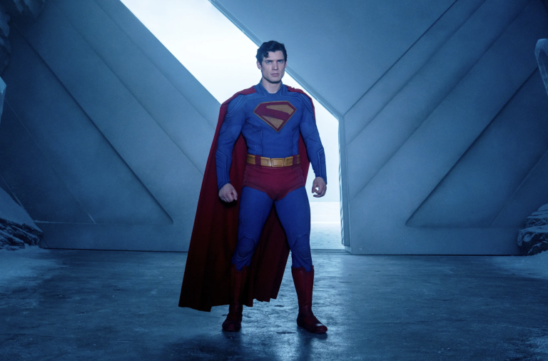 Superman stands firm in a bold stance inside an industrial-looking space.