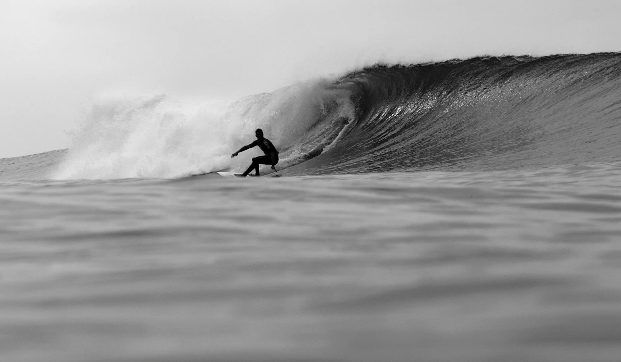 Black and white image of a male surfer riding the bottom of a cresting wave.